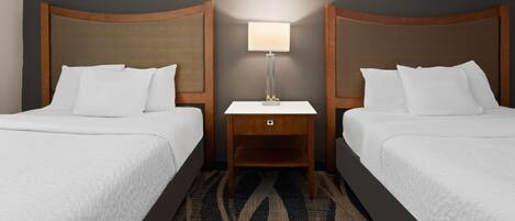 A hotel room with two beds, a nightstand with a lamp, and a patterned carpet.