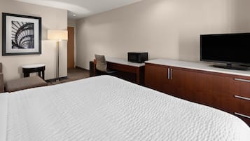 A hotel room with a large bed, a desk with a chair, a television, a lamp, and a framed picture on the wall.