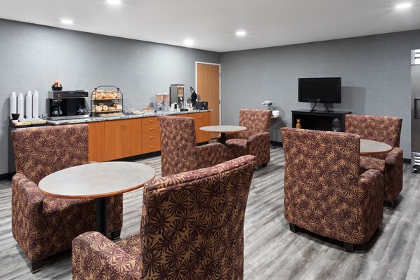 A hotel room with a kitchenette, a flat-screen TV, patterned armchairs, and a small round table.