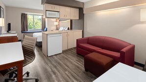 A compact hotel room with a kitchenette, a dining area, a red sofa, and a small table. - Americas Best Value Inn & Suites Racine (Mount Pleasant)