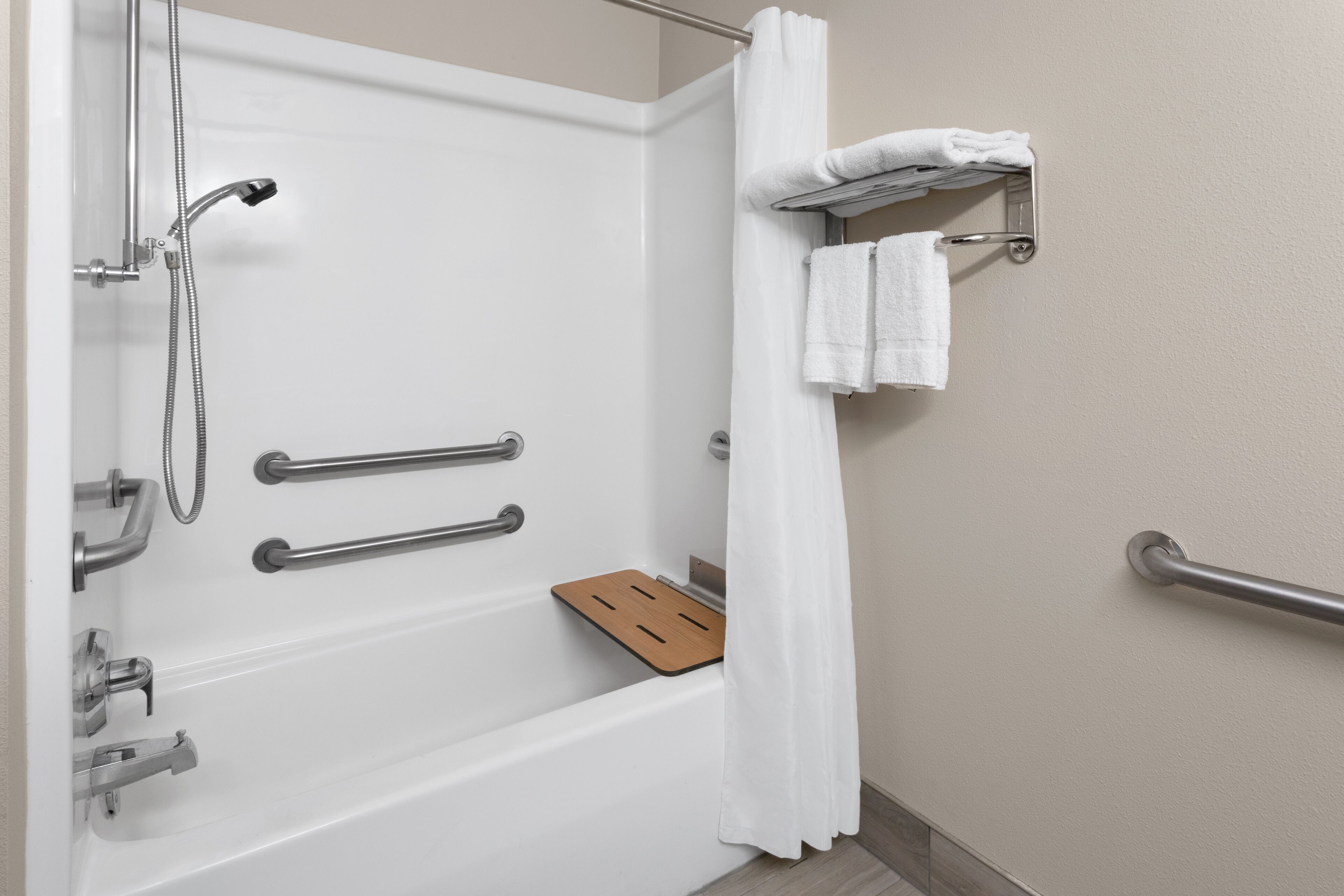 A bathroom with a white bathtub, grab bars, a showerhead, and a towel rack.