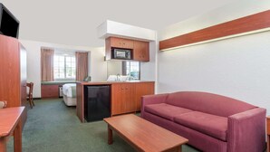 Ett kompakt hotellrum med ett litet kök, en soffa, ett träbord och en säng med utsikt genom fönstret.
