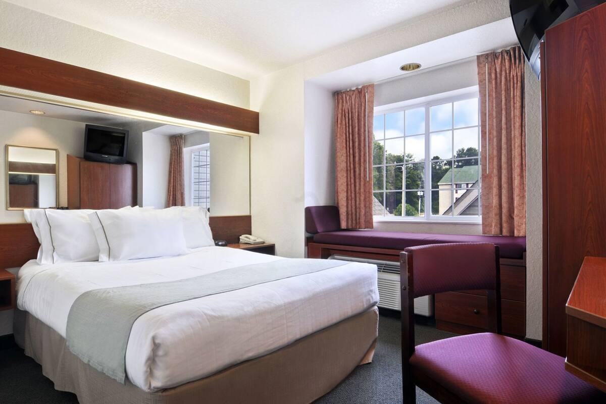 Ein Hotelzimmer mit Bett, Schreibtisch, Stuhl, Fernseher und einem Fenster mit Vorhängen.
