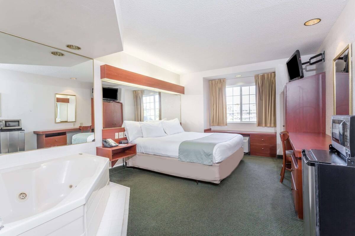 Ein Hotelzimmer mit einem großen Bett, einem Schreibtisch, einem Sessel, einem Fernseher, einer Mikrowelle und einem Badezimmer mit einer Badewanne.