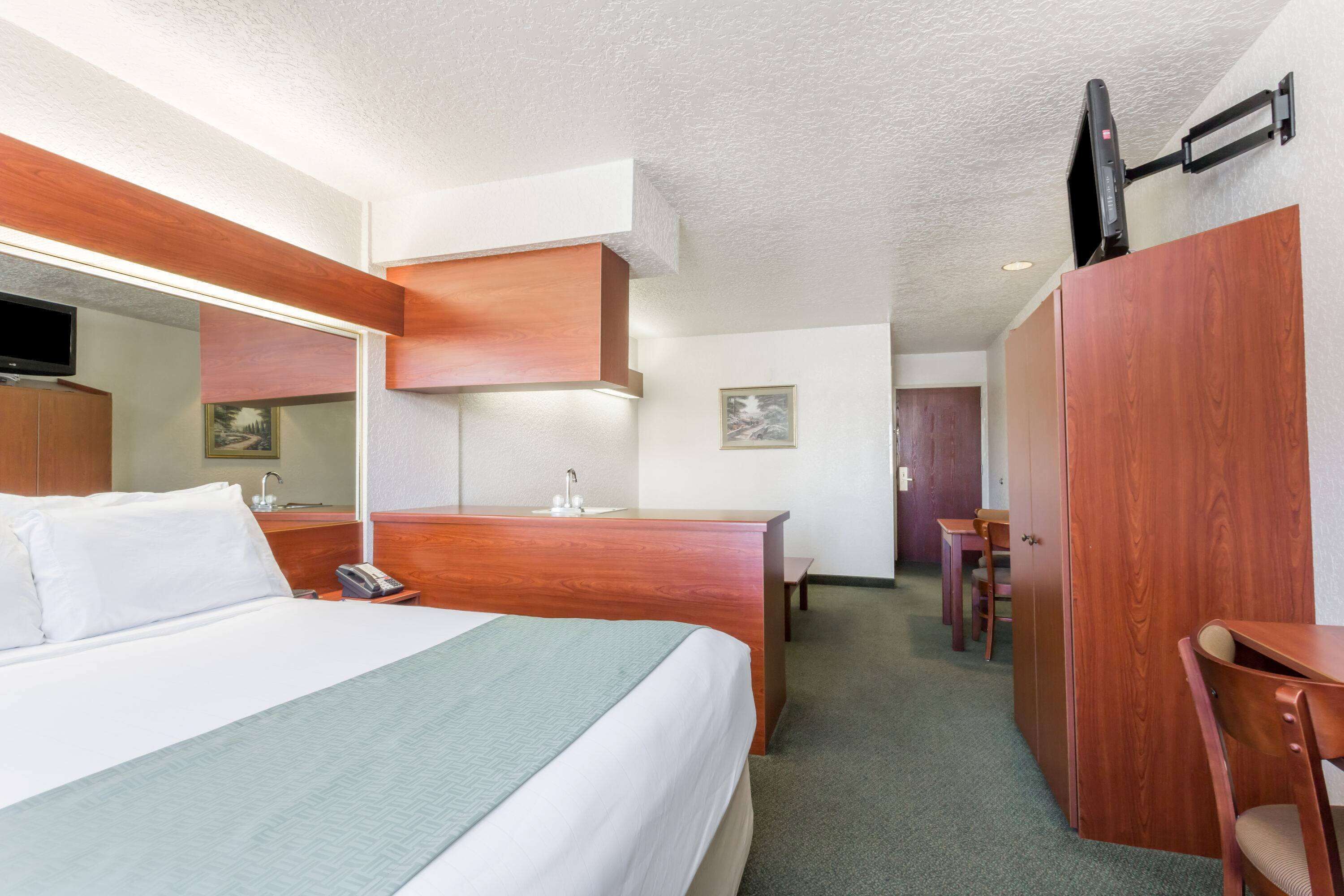 A hotel room with a bed, a desk, a chair, a mirror, and a television mounted on the wall.