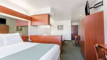Una habitación de hotel con cama, escritorio, silla, espejo y televisor montado en la pared.