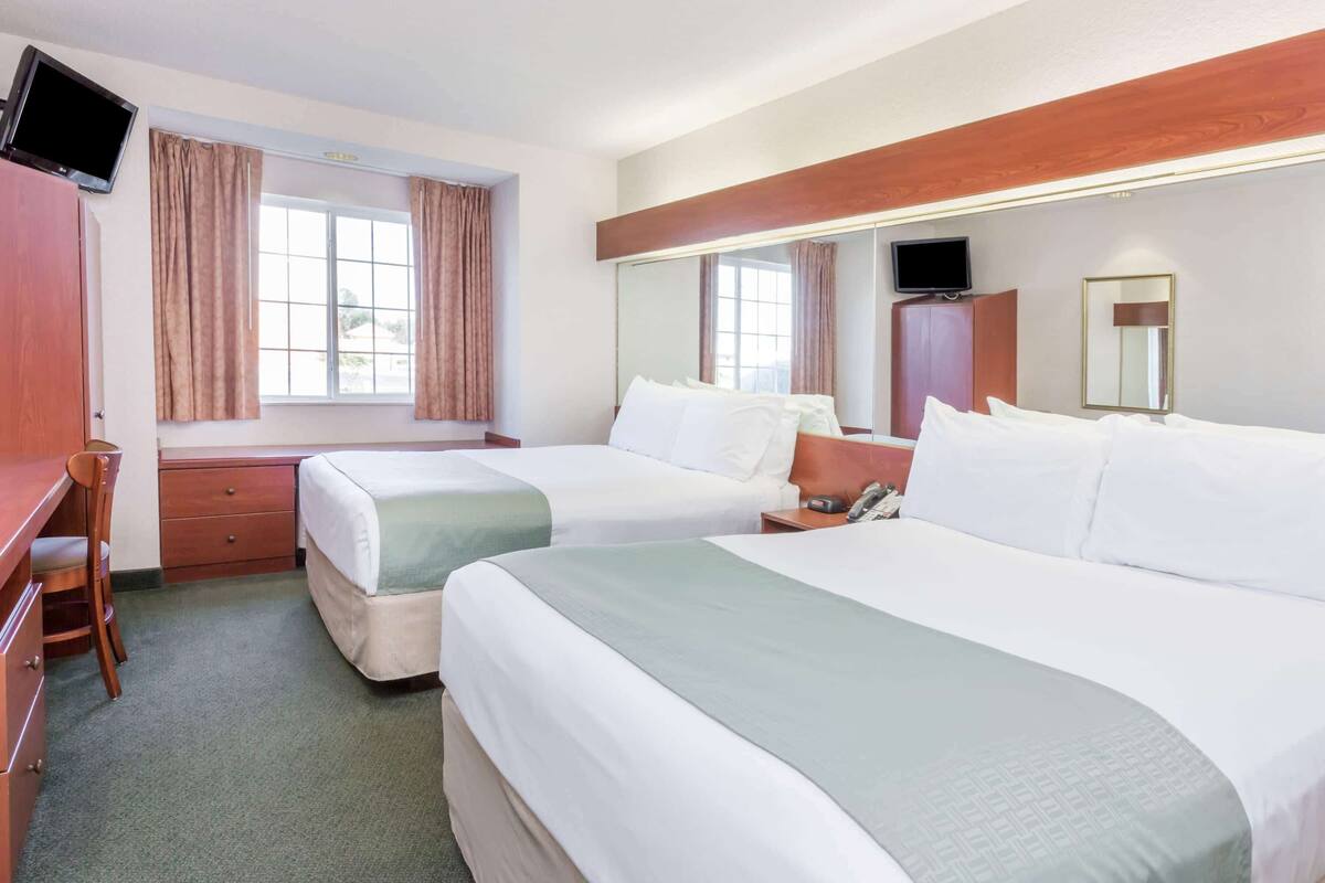 Ein Hotelzimmer mit zwei Betten, einem Schreibtisch, einem Sessel, einem Fernseher und einem Fenster mit Vorhängen.