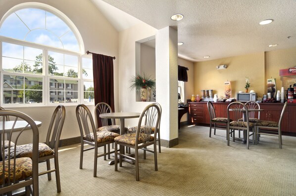 A hotel dining area with a large arched window, a bar area with a counter and bar stools, and a seating area with chairs and a table. - Microtel Inn & Suites by Wyndham Marianna (Marianna)