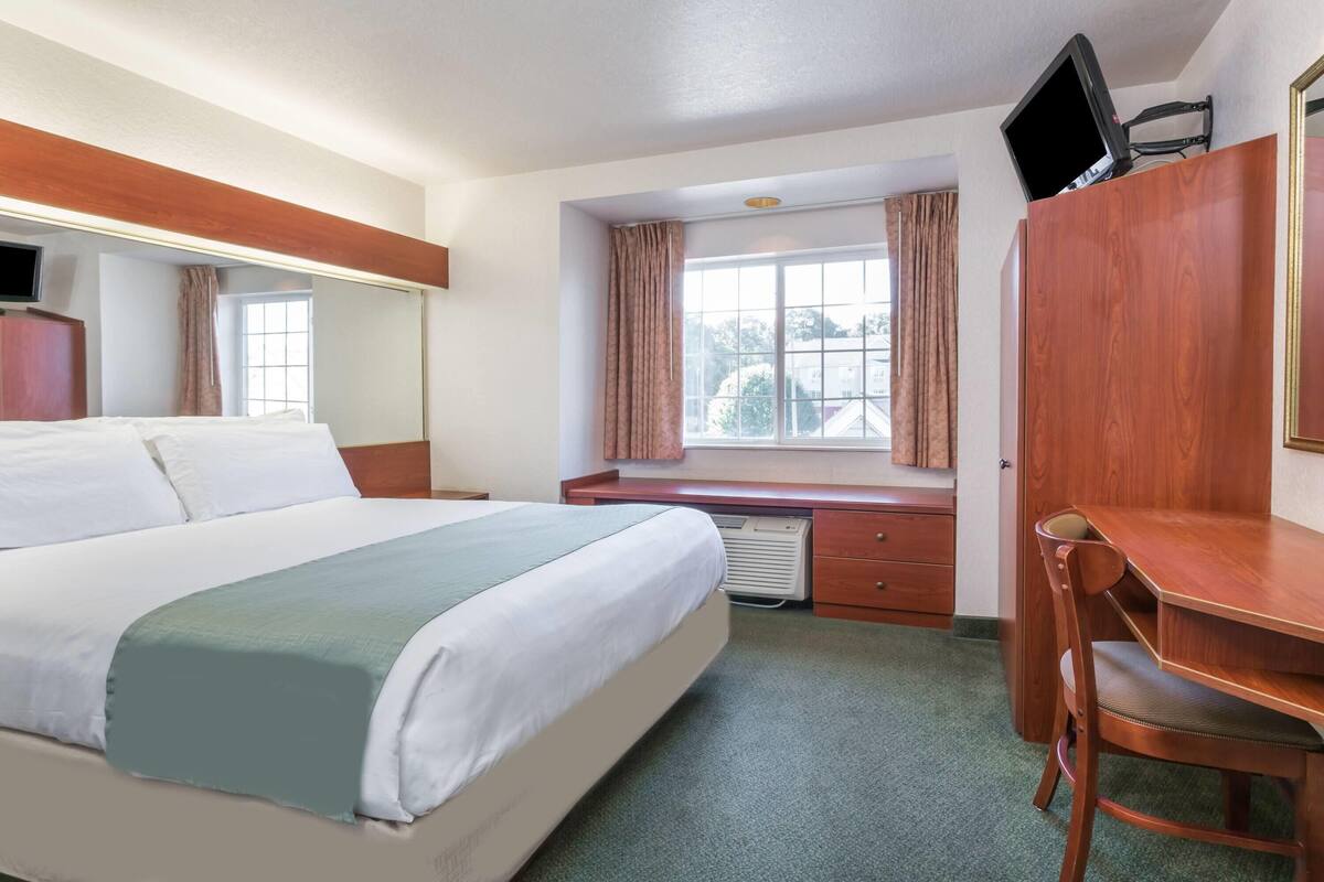 Ein Hotelzimmer mit Bett, Schreibtisch, Stuhl, Fernseher und einem fenster mit Vorhängen.