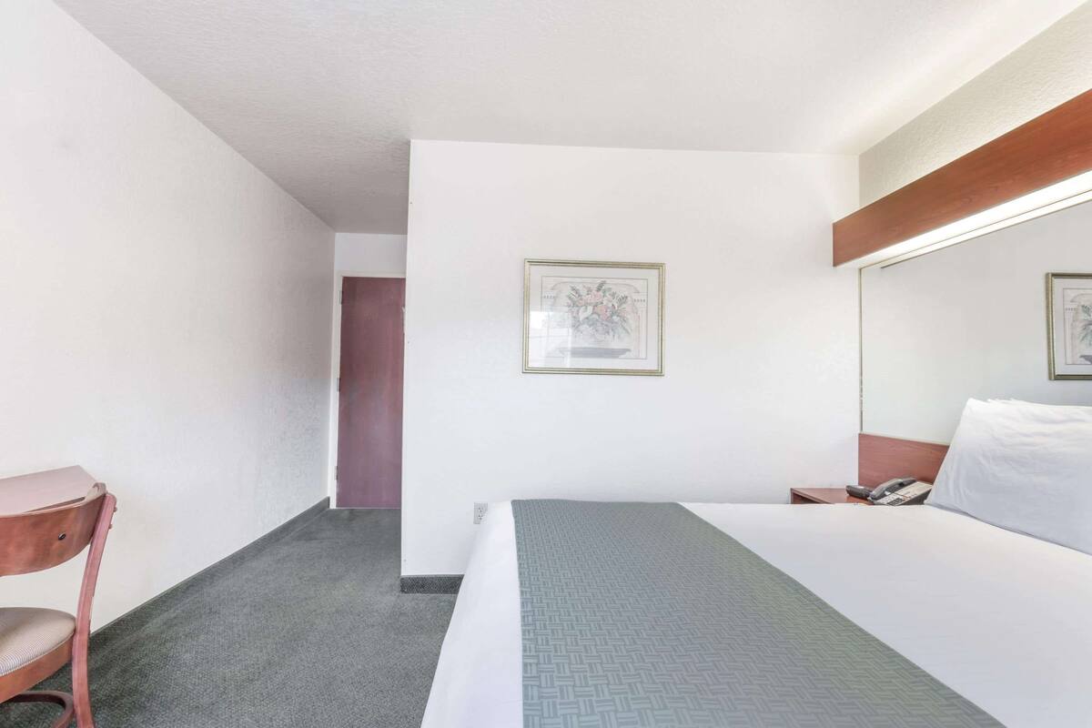 Ein Hotelzimmer mit Bett, Schreibtisch, Stuhl, Telefon und einem gerahmten Bild an der Wand.