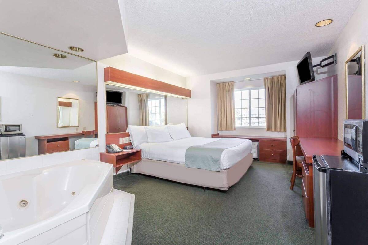 Ein Hotelzimmer mit Bett, Schreibtisch, Stuhl, Fernseher, Mikrowelle und einem Badezimmer mit Badewanne.
