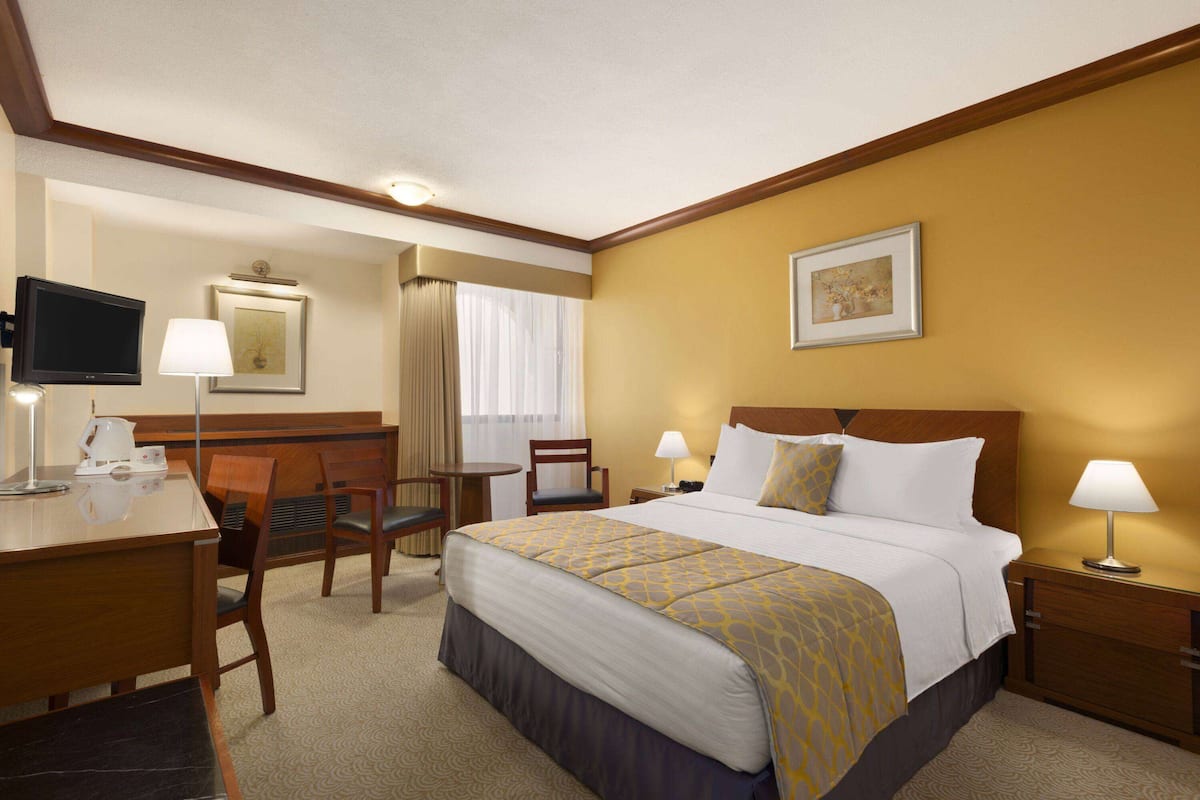 A hotel room with a bed, desk, chairs, a television, and a window with curtains.