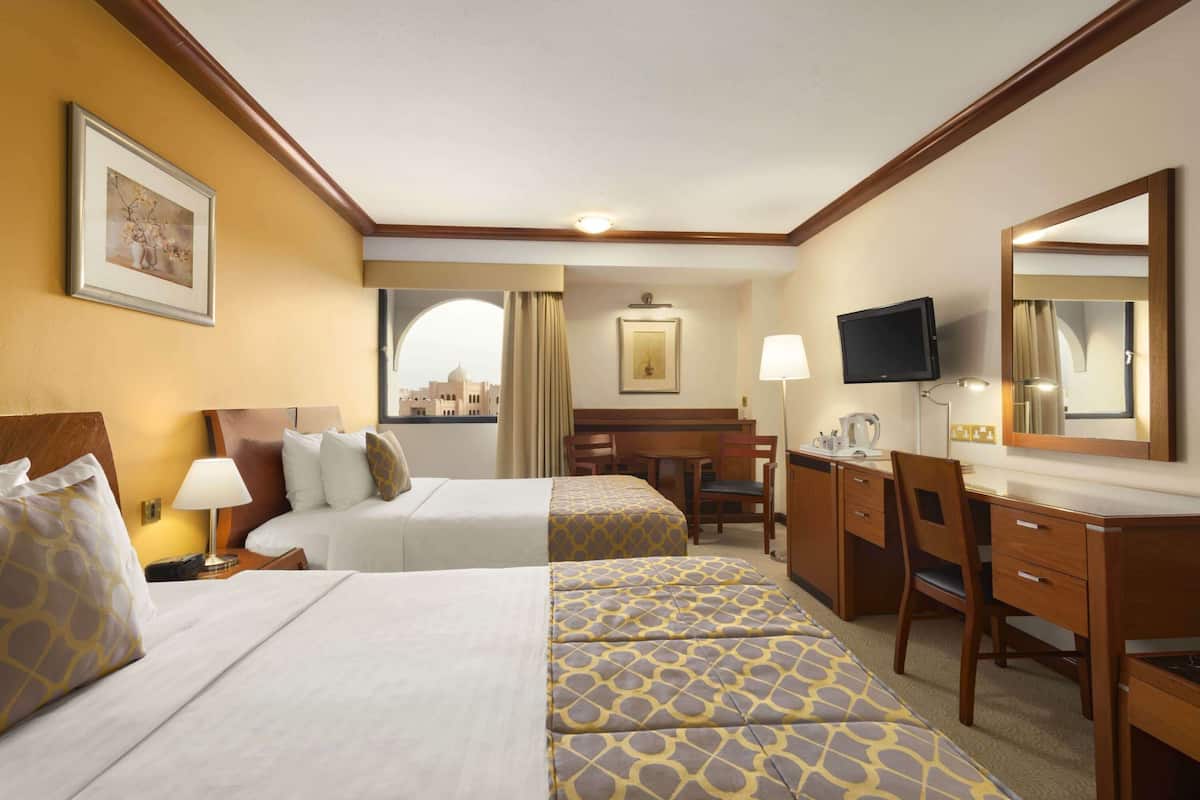 A hotel room with two beds, a desk, a chair, a television, and a window with a view of a building.
