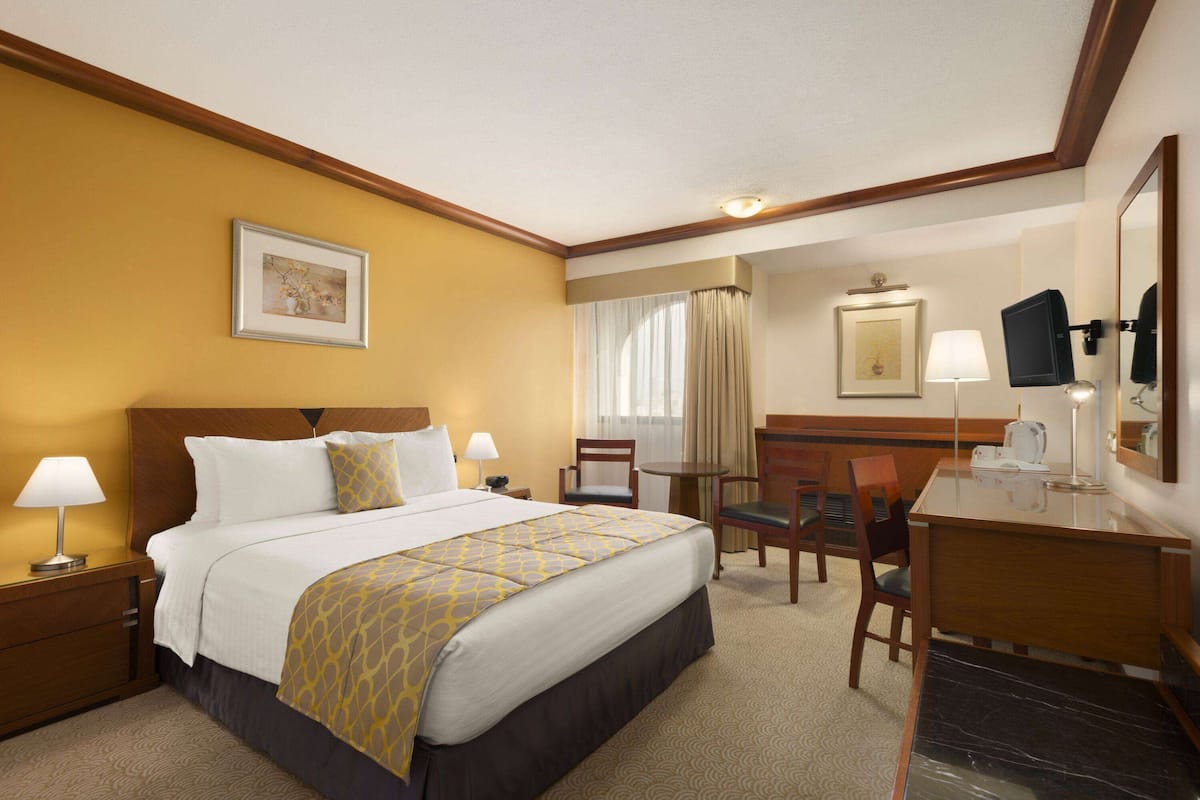 A hotel room with a bed, bedside tables, a desk, a chair, a lamp, a television, and a framed picture on the wall.