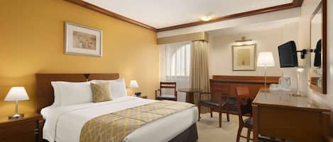 A hotel room with a bed, bedside tables, a desk, a chair, a lamp, a television, and a framed picture on the wall.