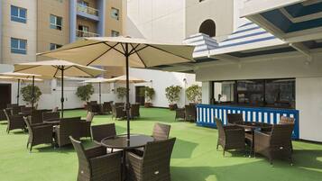 An outdoor patio with wicker furniture and umbrellas, a bar area, and a building with multiple windows and balconies.