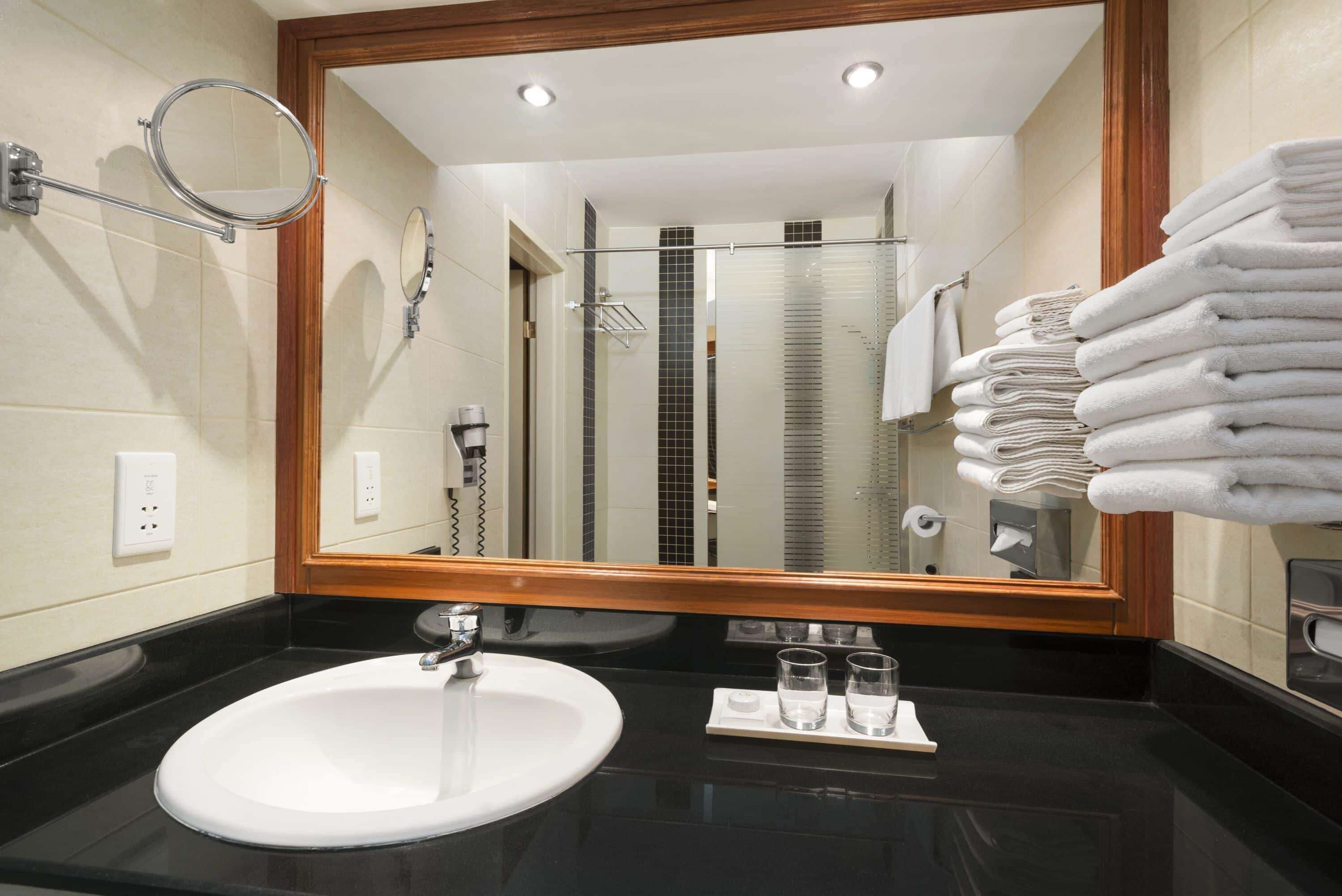 A modern bathroom with a large mirror, a sink, and a stack of white towels.