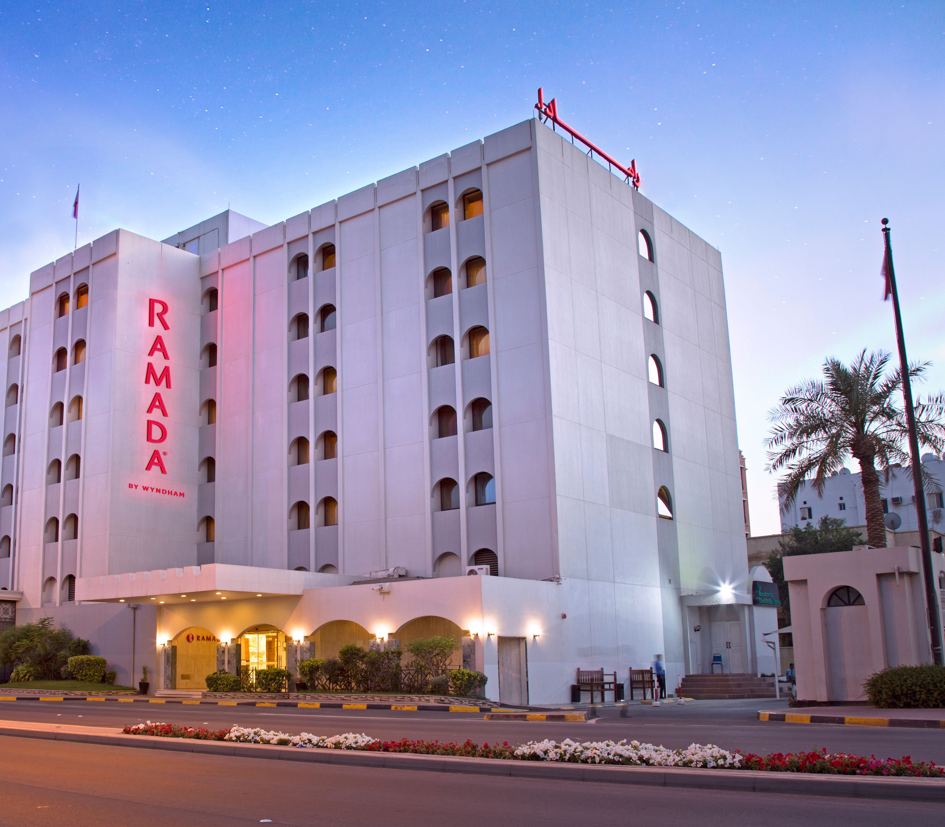 A modern hotel building with a prominent sign reading "RAMADA BY WYNDHAM".