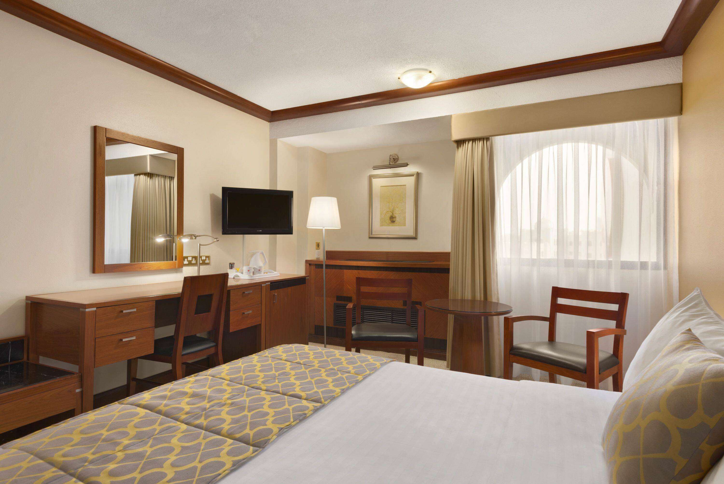 A hotel room with a bed, a desk, a chair, a television, and a window with curtains.