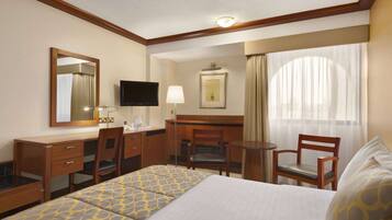 Habitación de hotel con cama, escritorio, silla, televisión y ventana con cortinas.