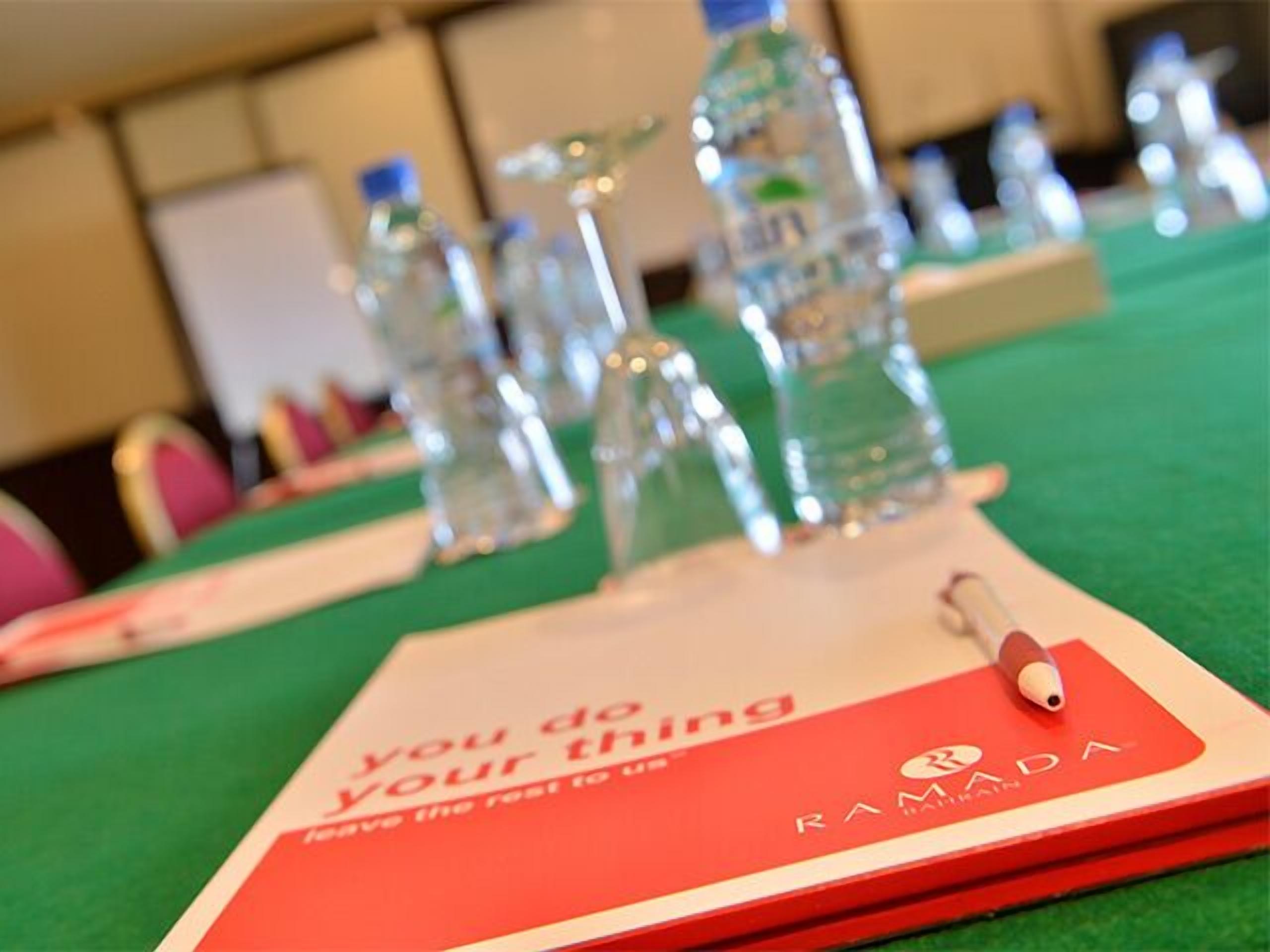 A conference table with water bottles and a red folder labeled "RAMADA" with the text "you do your thing" and "keep the rest to me."