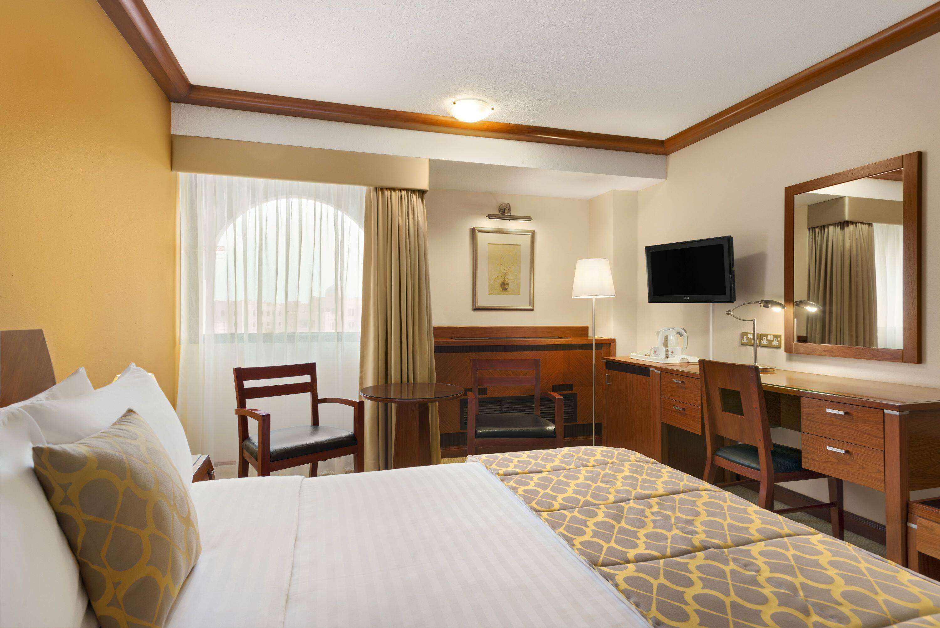 A hotel room with a bed, a desk, a chair, a television, and a window with curtains.