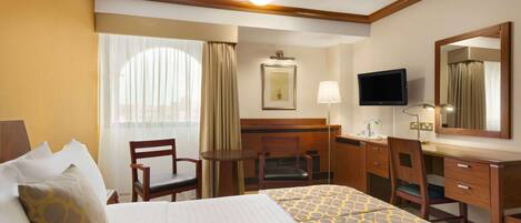 A hotel room with a bed, a desk, a chair, a television, and a window with curtains.