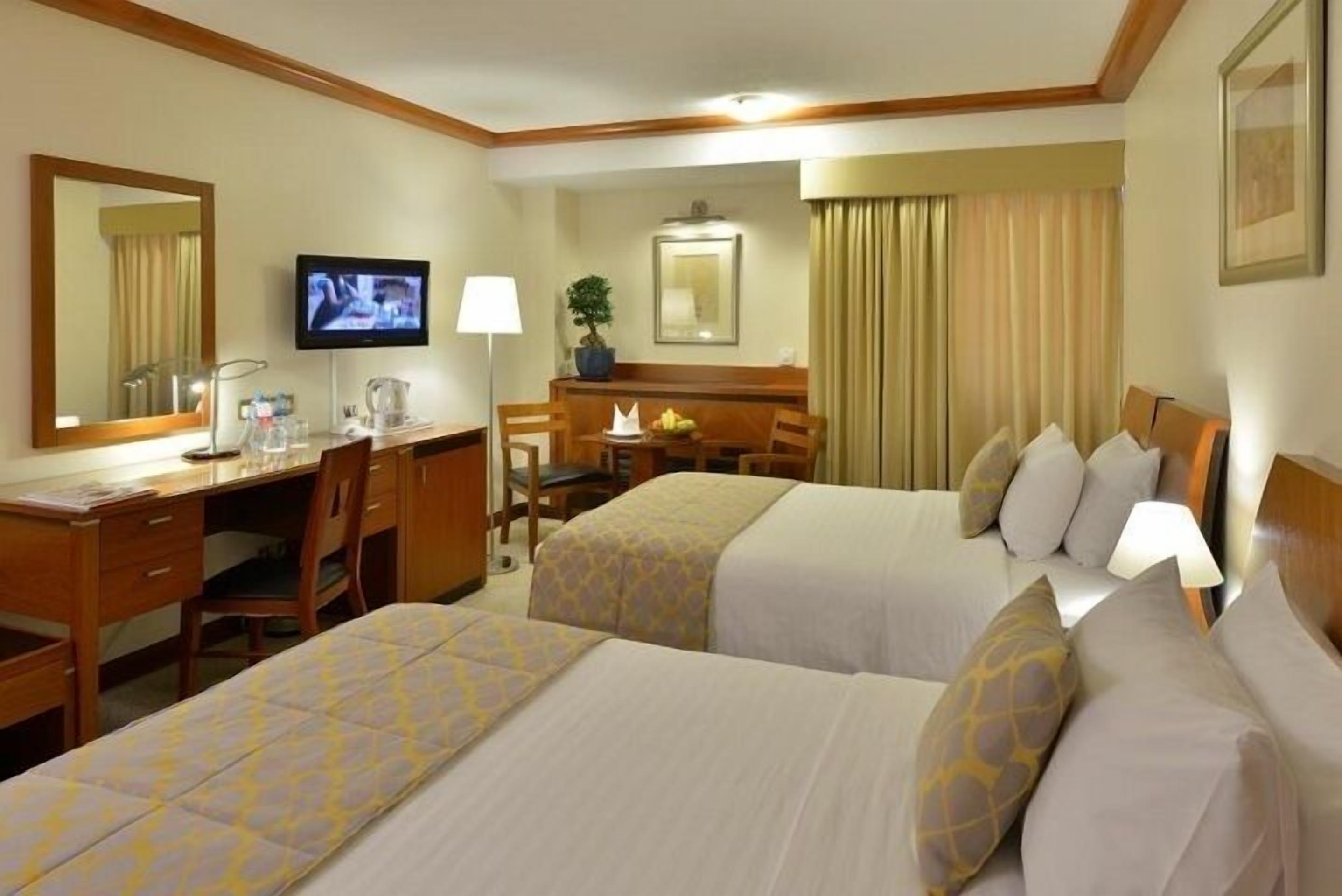 Habitación de hotel con dos camas, un escritorio, una silla, un televisor y un espejo.
