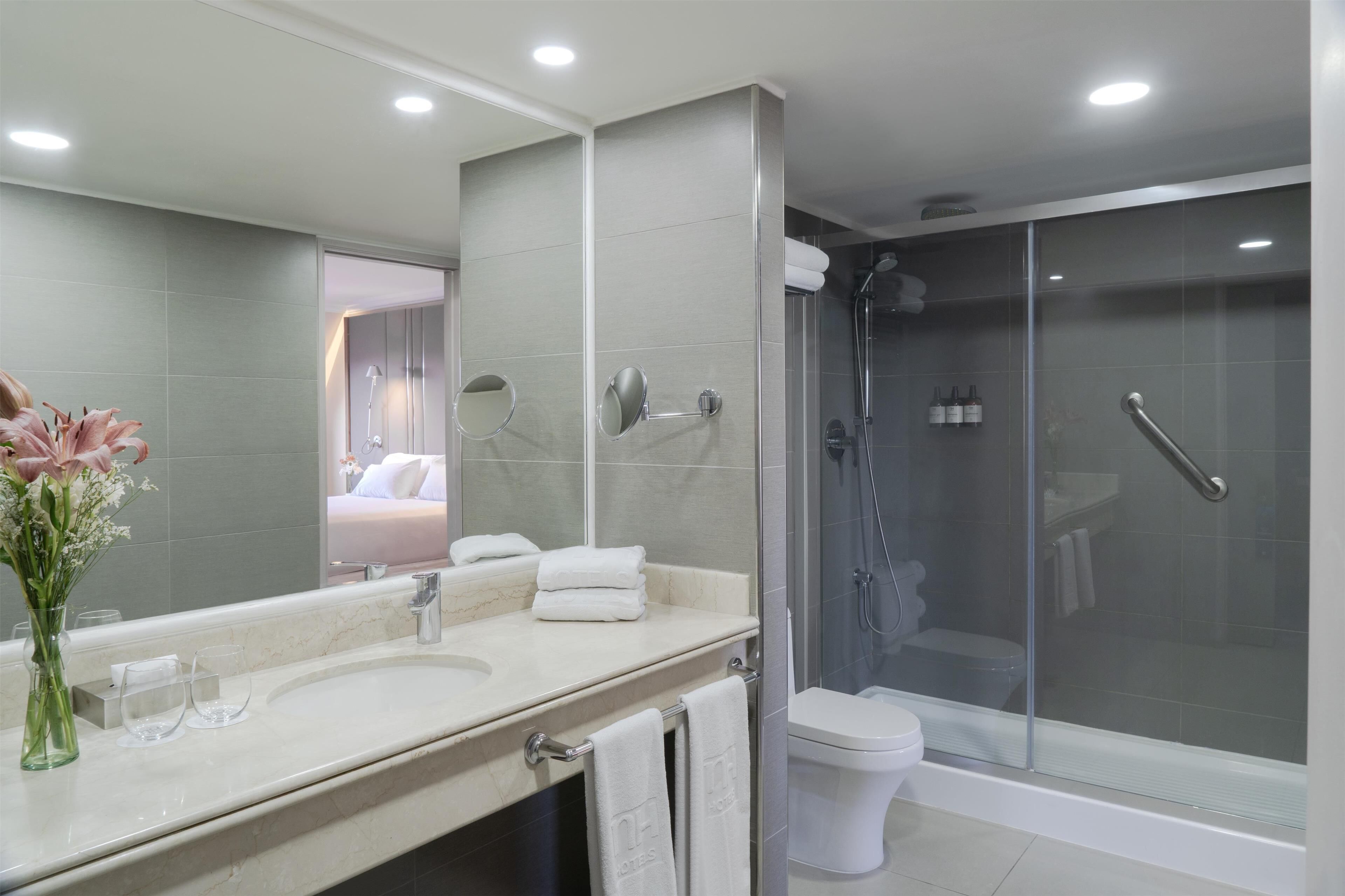 A modern bathroom with a large mirror, a sink, a toilet, and a glass-enclosed shower.
