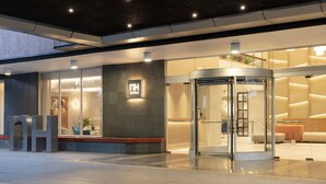 L’entrée d’un hôtel, avec une porte en verre, un comptoir d’accueil et un intérieur moderne visible à travers le verre.