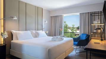 Una habitación de hotel moderna con una cama grande, un escritorio y una silla. Cuenta con una ventana con cortinas, un jarrón con flores y vistas a zonas verdes.