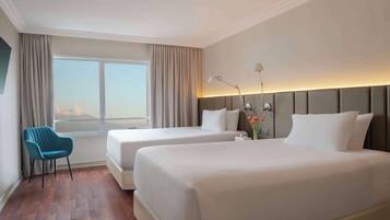 Habitación de hotel con dos camas, una silla, un ventanal con cortinas y una lámpara de noche.