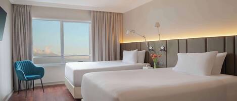A hotel room with two beds, a chair, a window with curtains, and a bedside lamp.