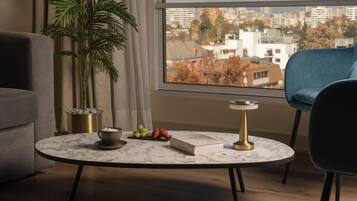 Un salon moderne avec une table basse ronde en marbre, un livre, une théière et un panier de fruits. Une grande fenêtre offre une vue sur le paysage urbain.