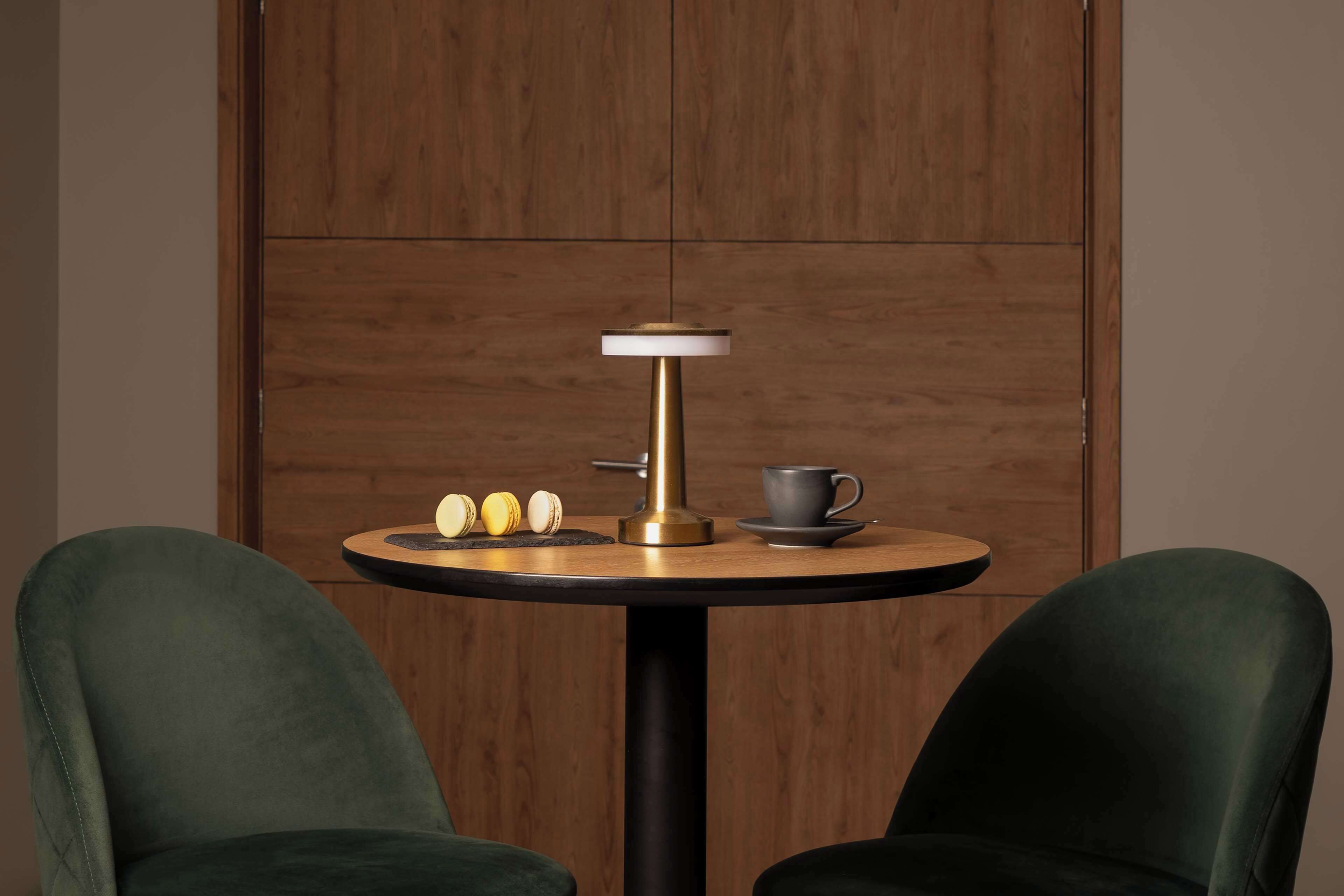 Una mesa redonda con una lámpara moderna, una taza y dos sillas en una habitación con paneles de madera.