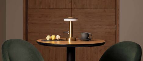 A round table with a modern lamp, a cup, and two chairs in a room with wooden paneling.