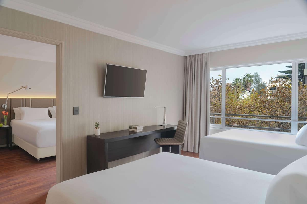 Une chambre d’hôtel avec un lit, un bureau avec une télévision et une fenêtre donnant sur des arbres.