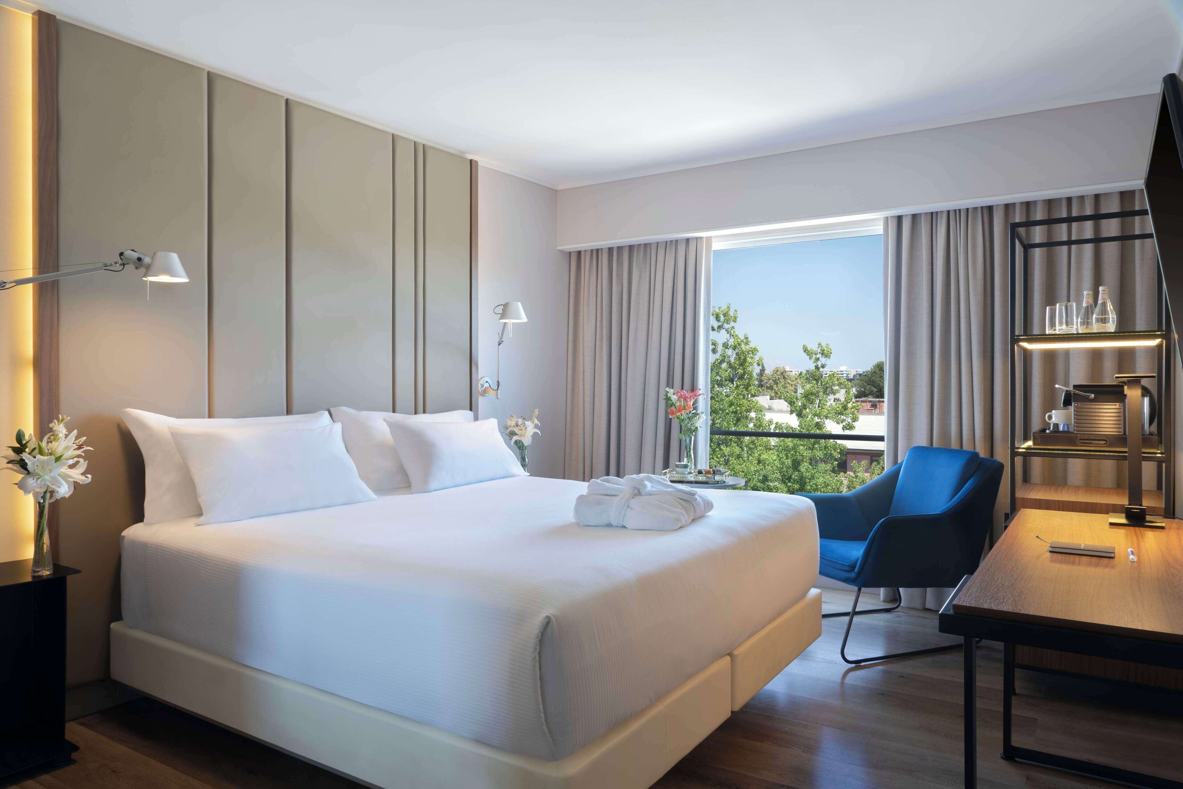 A hotel room with a large bed, a desk, a chair, and a view of the outdoors.