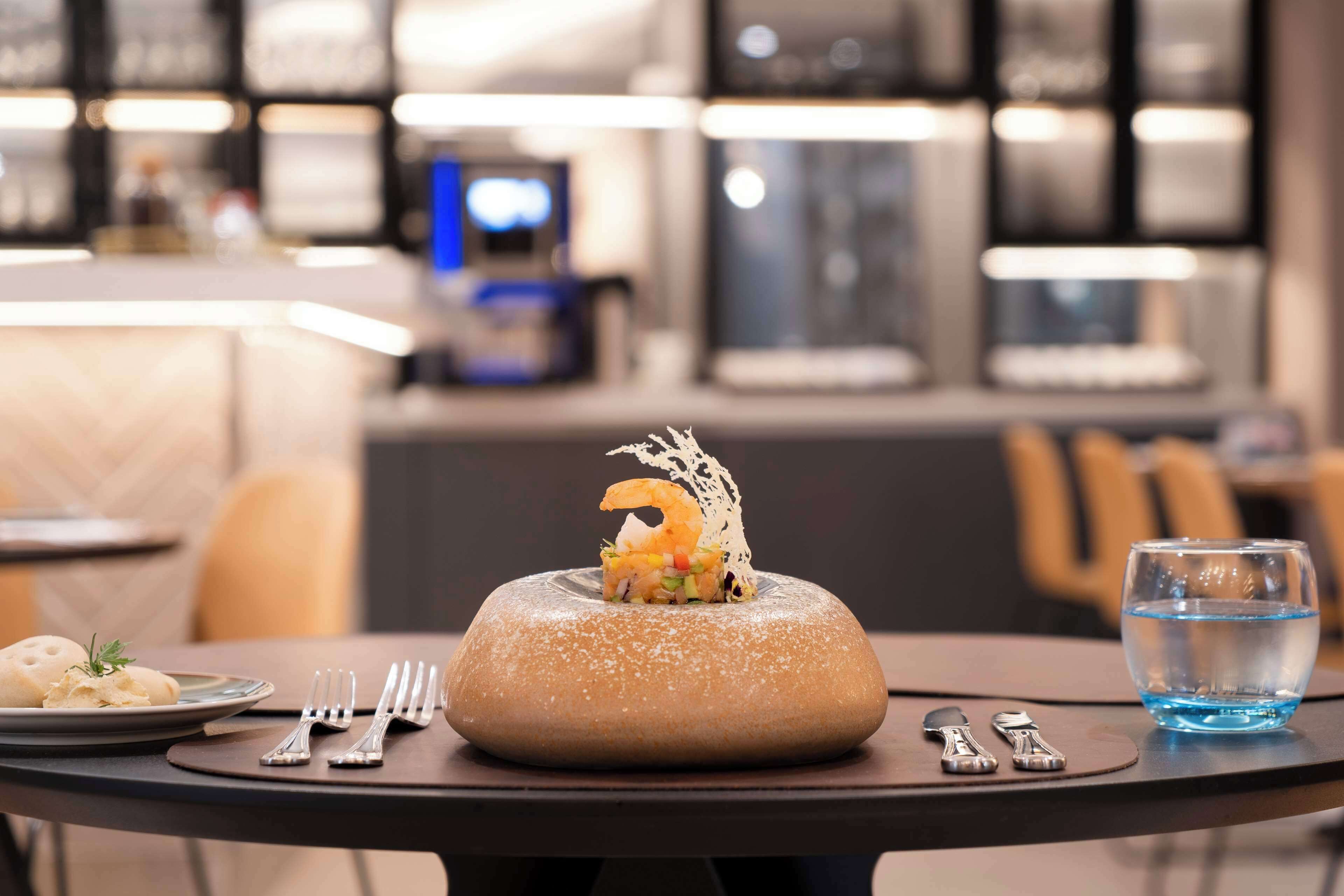 Una mesa de comedor con un centro de postres, cubiertos y un vaso de agua.