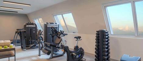 Un gimnasio con equipo de ejercicio, una banca y una ventana con vista a la montaña.