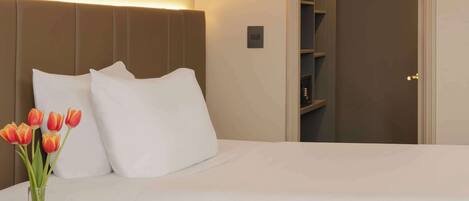 Habitación de hotel con dos camas, una mesita de noche con un jarrón de tulipanes, una lámpara y un armario con ropa colgada.
