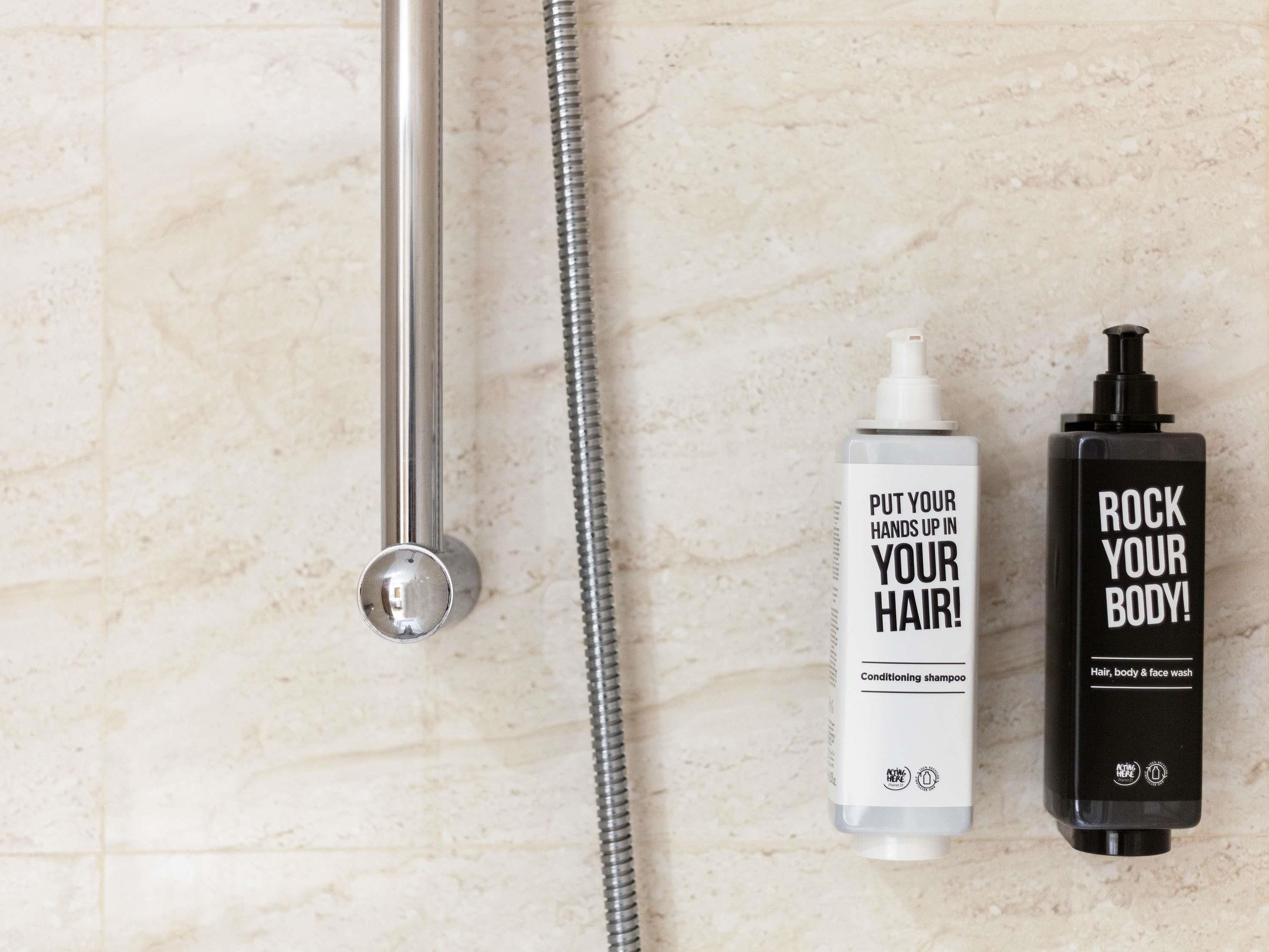 A bathroom with a shower, a white bottle of conditioning shampoo, and a black bottle of body wash.