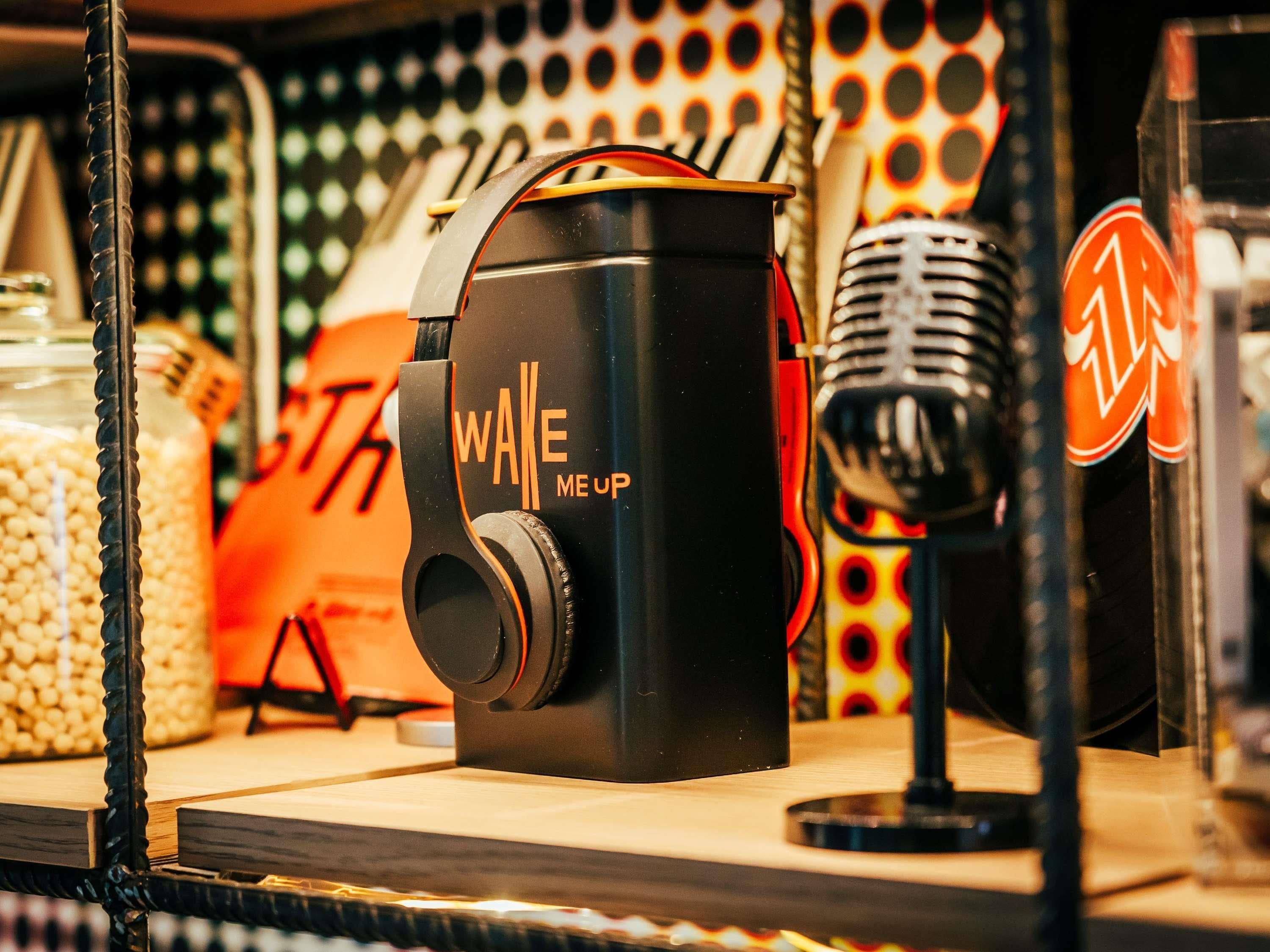 Ein Mikrofon mit 'WAKE ME UP' Branding, ein Vintage-Mikrofon und ein rotes und orangefarbenes Schild mit einem kreisförmigen Logo.