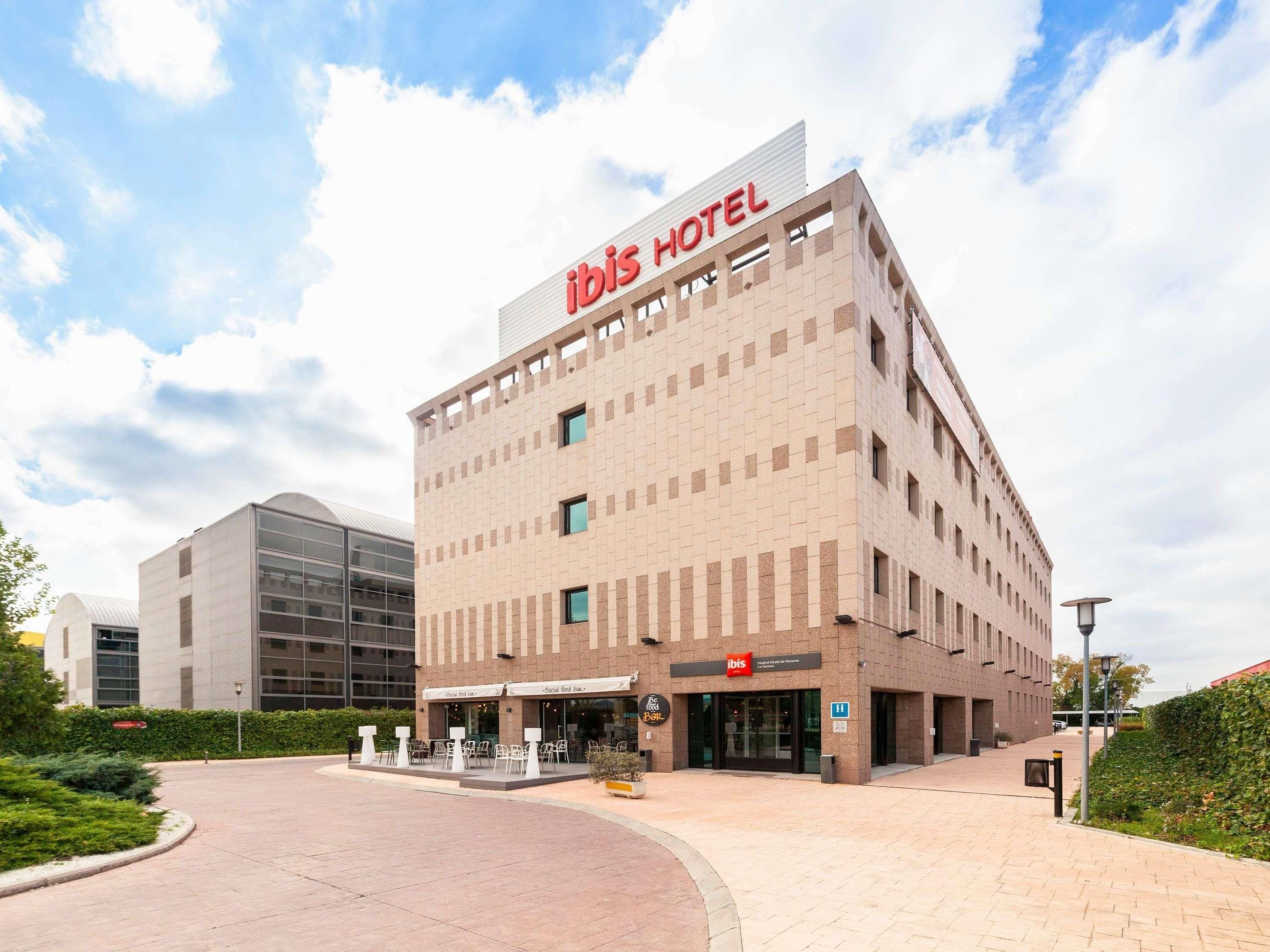 Edifici d'hotel amb un senyal prominent d''ibis HOTEL', un disseny arquitectònic modern i una zona d'entrada pavimentada.