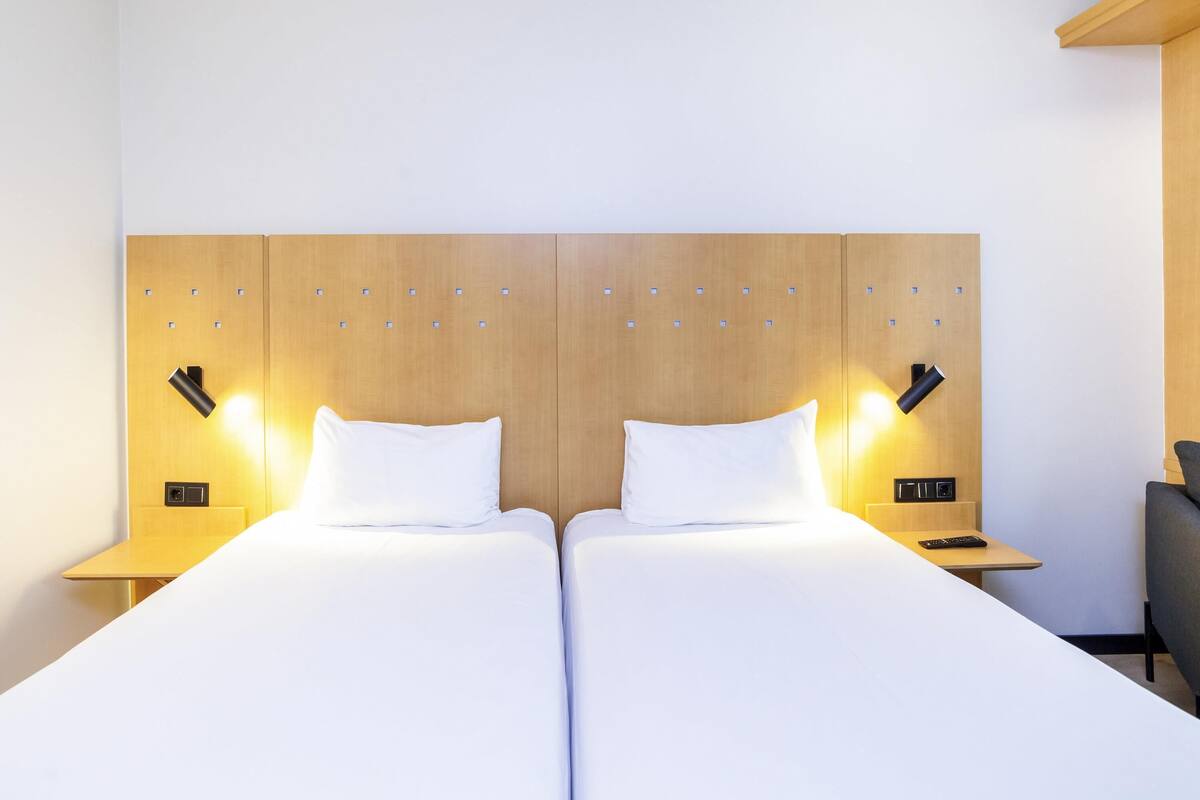 Una cama doble con cabecera de madera, dos mesitas de noche con lámparas y un escritorio pequeño con una silla.