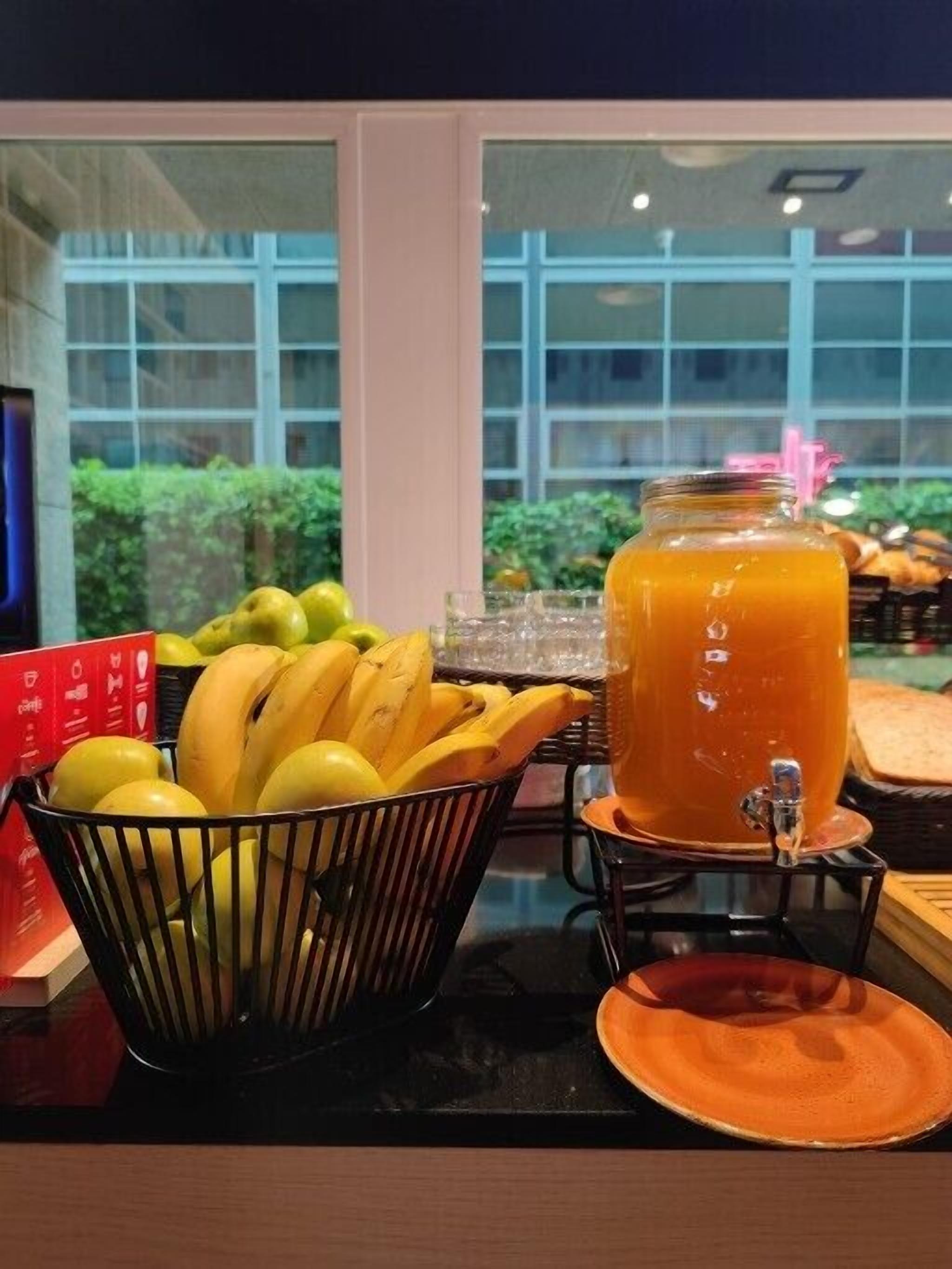 A breakfast setup with a fruit bowl, a juice dispenser, and a plate on a table.