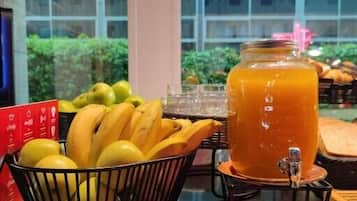 A breakfast setup with a fruit bowl, a juice dispenser, and a plate on a table.