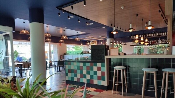 Un área de bar moderna con pared a cuadros, taburetes y lámparas colgantes.
