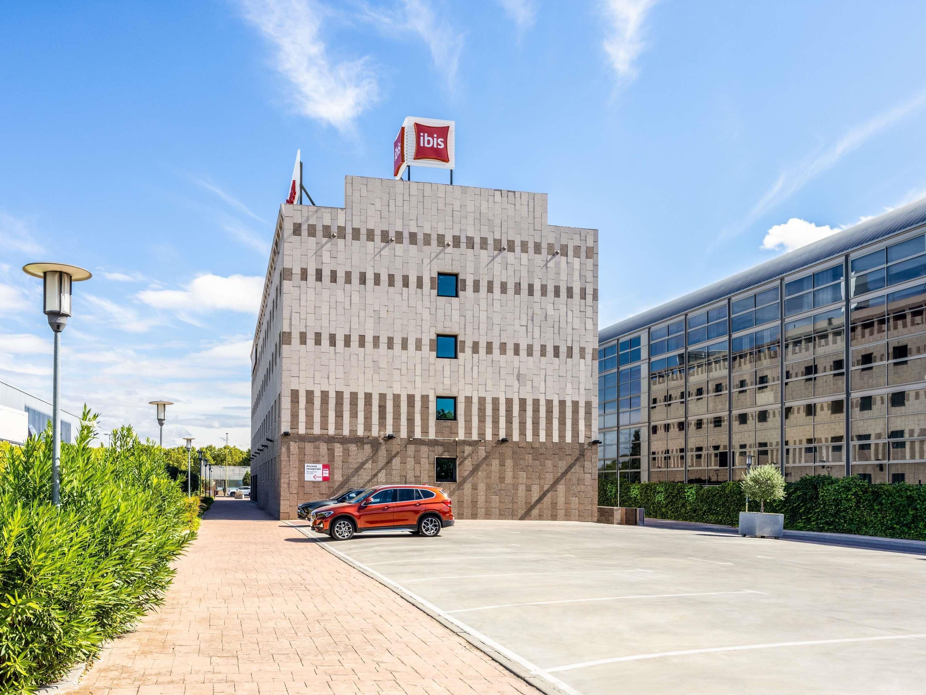 Un edificio moderno con una bandera, una zona de estacionamiento y un cielo despejado.