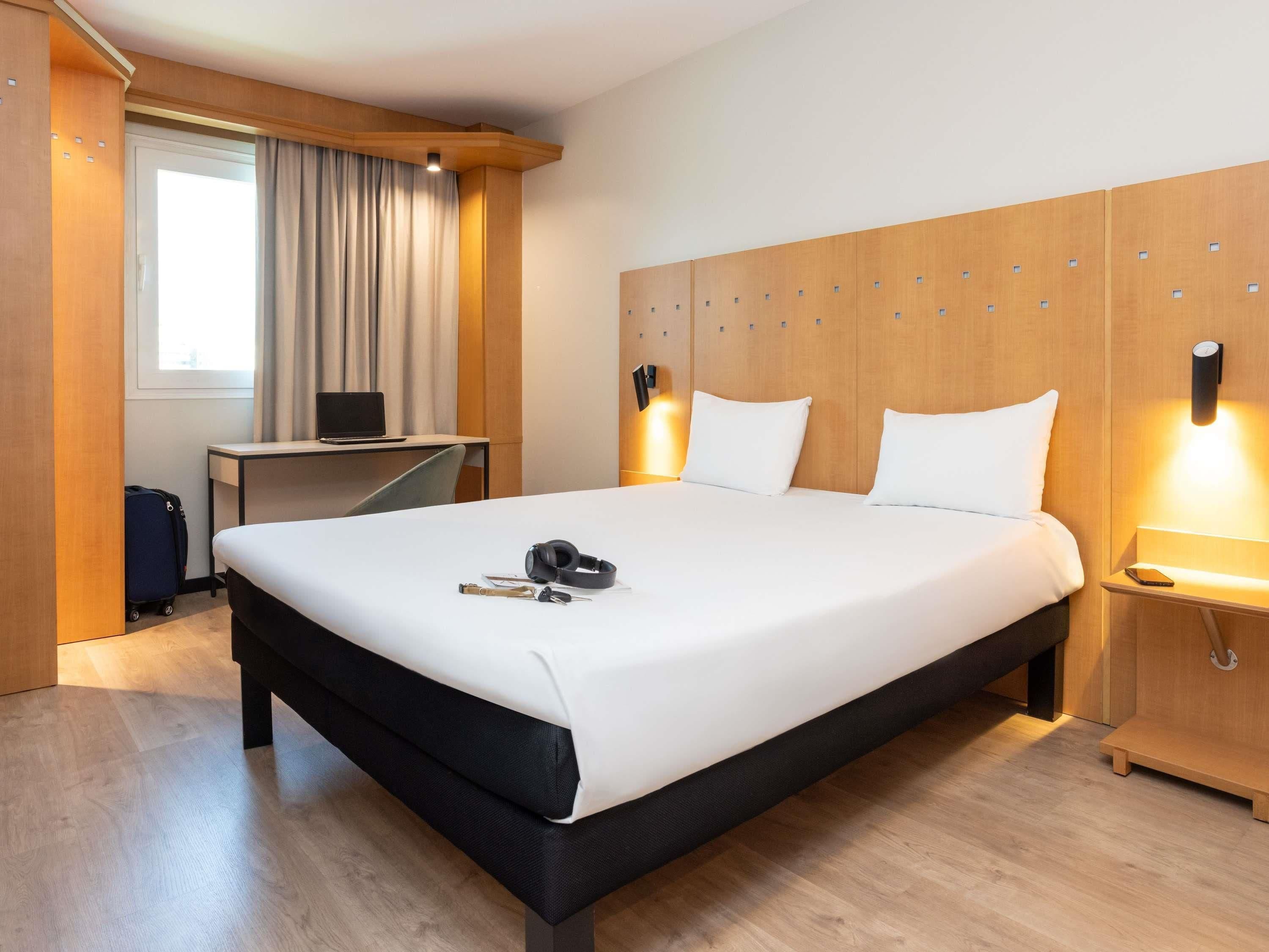 A hotel room with a large bed, a desk, a laptop, and a suitcase.